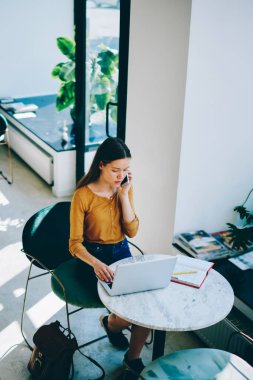 İçerideki meslektaşımla konuşmak için yeni bir akıllı telefon uygulaması aracılığıyla ararken çevrimiçi olarak çalışan konsantre kadın bilişim geliştiricisi, cep telefonuyla iletişim kuran ciddi bir metin yazarı
