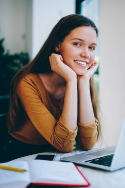 Üniversite kafeteryasında bilgisayar başında çalışırken yüzünde sevimli bir gülümsemeyle kameraya bakan başarılı kadın serbest yazar portresi. Kapalı alanda teknoloji kullanarak okuyan mutlu hippi kız.