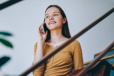 Başarılı bir bayan öğrenci üniversite merdivenlerinde oturuyor ve cep telefonuyla 4G bağlantısı ile olumlu bir konuşma yapıyor, mutlu bir kadın evde akıllı telefondan en iyi arkadaşıyla günlük kıyafetlerini giyiyor.