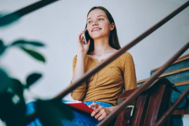 Başarılı bir bayan öğrenci üniversite merdivenlerinde oturuyor ve cep telefonuyla 4G bağlantısı ile olumlu bir konuşma yapıyor, mutlu bir kadın evde akıllı telefondan en iyi arkadaşıyla günlük kıyafetlerini giyiyor.