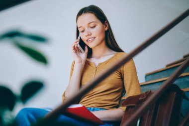 Üniversitede okuduktan sonra merdivenlerde oturup teknoloji ve iletişim konsepti olan akıllı telefondan arayan güzel zeki hippi kız bilgi okuyor.