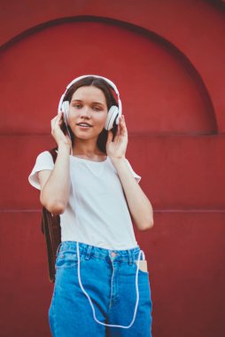 Modern stereo kulaklıklarla müzik dinleyen ve kameraya bakan çekici genç bir kadının portresi, modaya uygun giyinmiş güzel hippi kız açık havada yeni ekipmanlarla radyonun keyfini çıkarıyor.