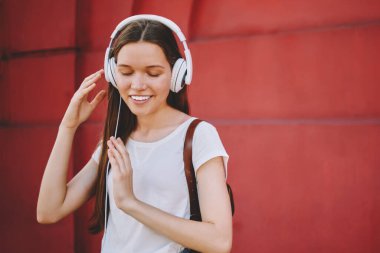 Yeni kulaklıkla müzik dinlemekten hoşlanan genç bir kız öğrenci ses kalitesinden tatmin olmuş gözlerini kapatıyor, kaygısız bir kadın dışarıda, duvarın yanında arkadaşını beklerken ses kitabı dinliyor.