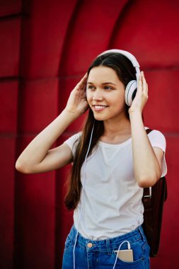Modayı takip eden mutlu hippi kız yüzünde sevimli bir gülümsemeyle kulaklıklardan medya çalma listesini dinlerken duvarın yanında duran ve radyo yayınından müziğin keyfini çıkaran neşeli meloman.