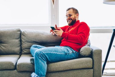 Mutlu genç çift gülerken akıllı telefon ve evdeki kablosuz bağlantı ile komik videolar paylaşıyorlar, evlilik birlikte eğleniyor ve sosyal ağlardaki içerikleri kontrol ediyor.