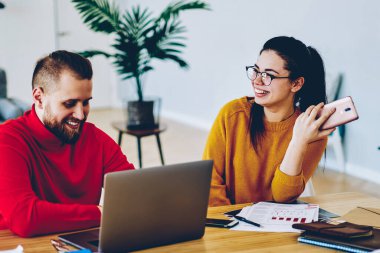 Erkek arkadaşıyla şakalaşan neşeli beyaz kadın modern teknolojiyi ve kablosuz interneti kullanarak araştırma yaparken gülümseyen beyaz çift tatil yapmayı planlıyor ve fikirleri tartışıyor.