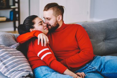 Genç, romantik bir erkek, genç karısını öpüyor. Kanepede birlikte vakit geçiriyor. Romantik bir çift, mutlu bir şekilde birlikte vakit geçiriyor.