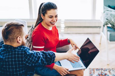 Dizüstü bilgisayar monitörünü işaret eden genç hippi evde boş zamanlarında ağ kurmak için web sitesine bakmış. Kocasıyla konuşurken gülen neşeli bir kadın web mağazasından eşyalar seçiyor.