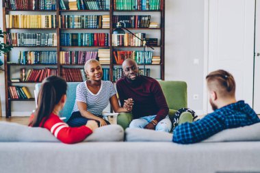 Mutlu genç evlilikler oturma odasında misafirlerle buluşuyor boş zamanlarında pozitif sohbet ediyorlar, hipsterlar birbirleriyle konuşuyorlar evdeki kanepede oturuyorlar, dizüstü bilgisayarla ön tarafta maket yapıyorlar.