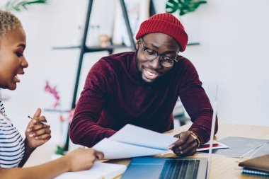 Koyu tenli erkek ve kadın meslektaşlar birlikte proje hazırlıklarını tartışıyor, Afrika kökenli Amerikalı iş arkadaşları masaüstünde dizüstü bilgisayarlarıyla oturup iş hakkında konuşuyorlar.