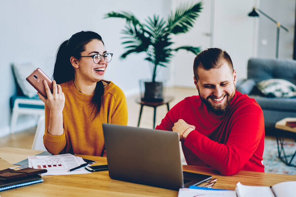 Позитивная пара хипстеров развлекается, работая вместе удаленно дома, используя современные технологии, веселый молодой мужчина и женщина смеются, строя планы на семейный бюджет общения