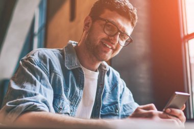 Gözlüklü, cep telefonunu elinde tutan ve kameraya bakan başarılı yeniyetmelerin portresi. Sohbet etmek ve iletişim kurmak için yeni akıllı telefon kullanan, gülümseyen bir ergen.