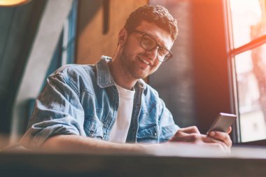 Gözlüklü, cep telefonunu elinde tutan ve kameraya bakan başarılı yeniyetmelerin portresi. Sohbet etmek ve iletişim kurmak için yeni akıllı telefon kullanan, gülümseyen bir ergen.