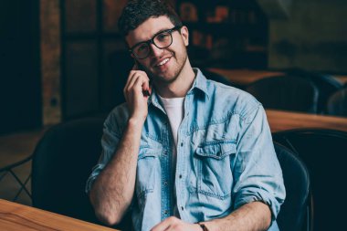 Kameraya bakıp iş arkadaşlarıyla konuşan neşeli hippi bir adamın portresi. Telefon görüşmeleri, cep telefonu uygulaması kullanarak arkadaşlarıyla olumlu gülümseyen bir mala.