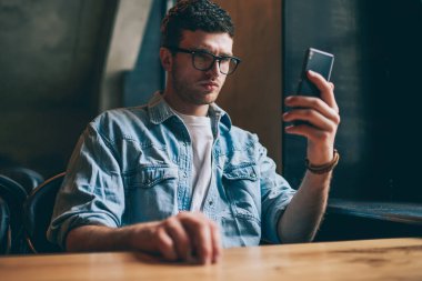 Akıllı telefon tutan ve sosyal haberler okuyan düşünceli bir hippi. Kot pantolonlu genç beyaz bir adam. İçerideki cep telefonundan multimedya uygulamasından izleniyor.