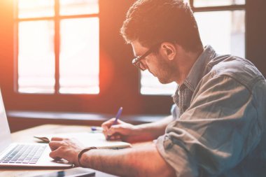 Genç milenyum erkek öğrencisi ev içi bilgisayar ve kablosuz ağ bağlantısı kullanarak ev ödevi arıyor, ders kitabında ilginç içerikler eklemek için kendi web sitesi veya web sayfasına yazı yazıyor