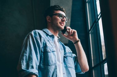 Gözlüklü pozitif erkek kullanıcı, cep telefonuyla arkadaşa telefon ediyor. Kablosuz internet bağlantısı var. Akıllı telefon konuşması sırasında pencereden bakan sıradan giyinmiş, güler yüzlü hippi adam.
