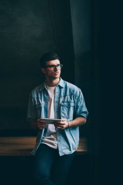 Gündelik görünüşlü düşünceli bir adam elinde dijital tabletle kampüsteki kablosuz internete bağlanmış, hipster adamın bilgi ve mesajlaşma için modern dokunmatik pedi kullandığını düşünüyor.