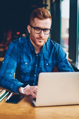 Portre grafik tasarımcı ile Kızıl saçlı çalışma serbest dizüstü bilgisayar, kablosuz internet'e bağlı. Üniversitesi'nde oturan netbook üzerinde kurs için metni yazarak gözlük yetenekli öğrenci