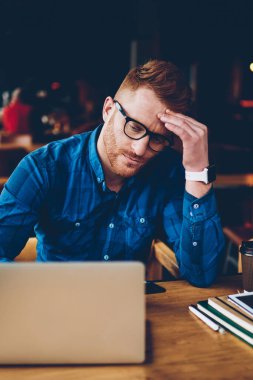 E-öğrenme dizüstü bilgisayar, gelen yorgun kırmızı saçlı yetenekli öğrenci gözlük içinde tükenmiş. İzlerken sıkıcı webinar modern netbook, ahşap masa kafede kahve ile oturmak, genç adam