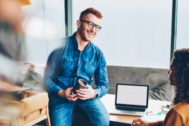 Neşeli iki çalışanı beyaz mimar ve Afrika kökenli Amerikalı tasarımcı kahve molası sırasında şık ofiste birbirleriyle iletişim kurmak. Boş ekran alanı ile modern dizüstü bilgisayar