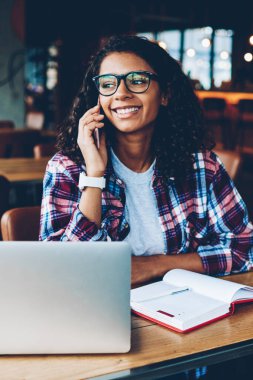 Neşeli koyu tenli öğrenci dostu mobil konuşma dizüstü bilgisayar vasıl okul sırası oturan smartphone cep telefonu ile mutlu. Hücresel Kitaplığı'nda okuyan iletişim olumlu Afro-Amerikan teen