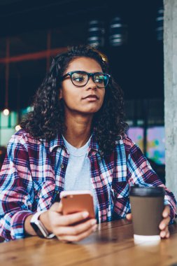 Afro-Amerikan hipster kız arkadaşına smartphone cep telefonu ile sms mesaj yollama mola sırasında git kahve ile dinlenme Eyewear. Koyu tenli teen el kitabı ile masaüstünde oturan telefon ile