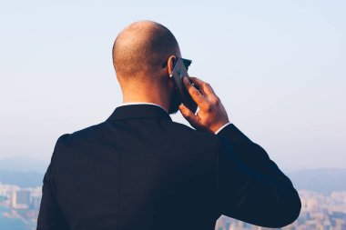 Arkadan görünüşü önemli iş konuşmayı meslektaşım yolu ile yüksek gökdelenler ile modern şehir güzel manzarayı smartphone aygıt ile siyah şık takım elbise giymiş erkek girişimci