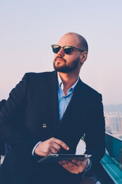 Kendine güvenen erkek gurur CEO'su siyahlar giymiş şık takım elbise ve dijital dokunmatik holding güneş gözlüğü ile yüksek hızlı internet duran cam balkon teras yakınındaki kopyalama alanı alanı iş bilgi için yastık