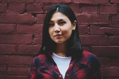 Kapalı moda esmer hippi kız portresi duvarın yanında duruyor ve kendine güvenen 20 'li yaşlarda şık şık giyinmiş, dışarıda kameraya bakan çekici Asyalı genç kız pozu veriyor.