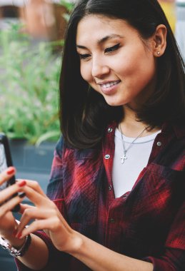 Yeni modern cep telefonuyla fotoğraf çeken mutlu esmer kadın, elinde cep telefonu tutan başarılı Asyalı hippi kız kameraya bakıyor ve başvuru formunu kullanarak arkadaşıyla video görüşmesi yapıyor.