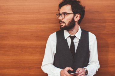 Zarif giyimli yakışıklı hippi arkadaşlarıyla cep telefonuyla iletişim kurarken yüzünü çeviriyor. Sosyal ağlardaki profili güncellemek için modern akıllı telefon cihazı kullanan genç trend adam.