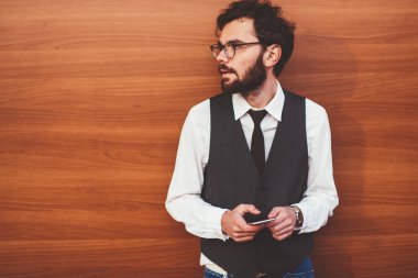 Zarif giyimli yakışıklı hippi arkadaşlarıyla cep telefonuyla iletişim kurarken yüzünü çeviriyor. Sosyal ağlardaki profili güncellemek için modern akıllı telefon cihazı kullanan genç trend adam.