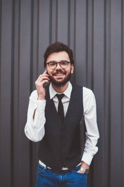 Olumlu uluslararası telefon görüşmeleri sırasında kameraya bakan neşeli hipster adamın yarım boy portresi. Gözlüklü adamın tanıtım alanında gezinme bağlantısını kullanması.