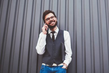 Gülümseyen hippi adam telefon uygulaması aracılığıyla arkadaşa telefon ediyor. Reklam alanında gezinme bağlantısını kullanıyor. Modayı takip eden giysili mutlu beyaz adam fotokopi alanı yakınlarında akıllı telefon konuşması yapıyor.