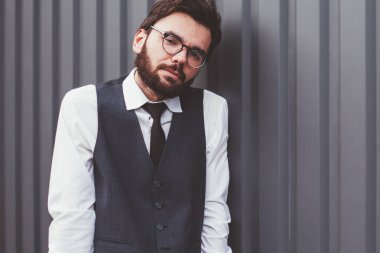 Gözlüklü, beyaz tenli, gözlüklü, tanıtım arkaplanının yanında duran ve dışarıdaki kameraya bakan, fotokopi alanının yakınında poz veren, günlük giyinen genç bir erkek öğrenci.