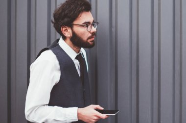 Moda kıyafetli genç adam elinde modern akıllı telefon cihazıyla fotokopi alanının yakınında çağrı bekliyor. Kafkasyalı hippi adam dışarıda mesajlaşmak ve sohbet etmek için yeni cep telefonu kullanıyor.