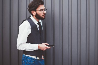 Moda kıyafetli genç adam elinde modern akıllı telefon cihazıyla fotokopi alanının yakınında çağrı bekliyor. Kafkasyalı hippi adam dışarıda mesajlaşmak ve sohbet etmek için yeni cep telefonu kullanıyor.