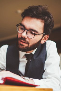 Genç sakallı erkek öğrenci, üniversite kampüsünde otokopi çekmek için zaman harcar. Not defterine makale yazarken. Gözlüklü beyaz tenli hippi, eğitim kitabında organizasyon planını not eder.