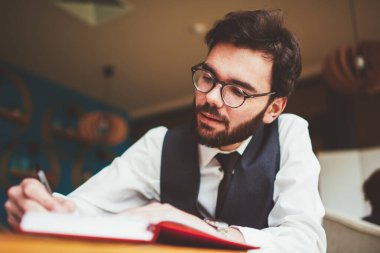 Genç sakallı erkek öğrenci, üniversite kampüsünde otokopi çekmek için zaman harcar. Not defterine makale yazarken. Gözlüklü beyaz tenli hippi, eğitim kitabında organizasyon planını not eder.