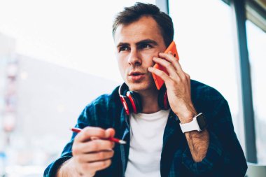 Durulması yakışıklı zeki erkek öğrenci kapalı sınavlara hazırlanırken online konsültasyon sahip trendy kıyafetler giymiş. İyi görünümlü yaratıcı blogger kafede oturan arkadaşları ile konuşurken