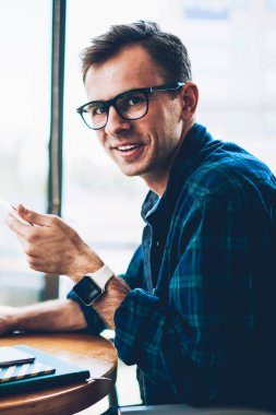 Yarım uzunluk portre serin gözlük kafede uzak çalışması sırasında modern teknoloji kullanılarak yakışıklı neşeli erkek geliştirici. Yazılım laptop güncelleştirilirken kameraya bakarak gülümseyen hipster adam