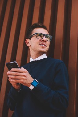 Pozitif delikanlı modern cihaz ve iyi bir ruh hali ile kentsel ayarda dinlenme zevk şık kıyafeti giymiş. Mutlu erkek kişi yaz Sokağı'nda eğlence ve sosyal ağ iletileri gönderme