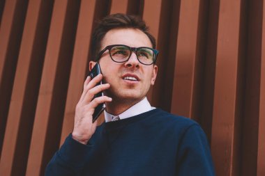 Yakışıklı olumlu erkek öğrenci şık Eyewear yaz telefonla konuşma sırasında sokak vasıl dinlenme zevk. Smartphone uygulama açık havada üzerinden mobil konuşmayı genç gülümseyen adam