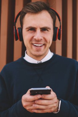 Yarım uzunlukta boş vakit yaz Street ve modern teknoloji kullanılarak yakışıklı neşeli erkek öğrenci portresi. Mutlu adam kulaklıklar ile en sevdiğiniz müzik dinlerken eğleniyor