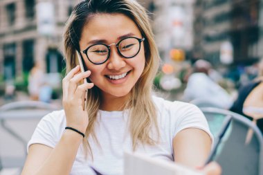 Şehir merkezinde, mutlu kız öğrencinin yurt dışında ucuz tarifeler ile görüşmeleri yapmaktan gezici bağlantısı kullanarak kafede otururken planları tartışırken arkadaş ile iletişim zevk neşeli Asyalı kız