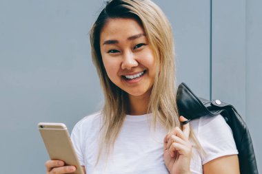 Kopyalama alanı alanı reklam yolu ile hücresel aygıt, online iletileri gönderme için yakın fotoğraf makinesi smartphone ile gülümseyen genç Çince blogger kadın poz neşeli sarışın Asyalı kız portresi yarım uzunluk