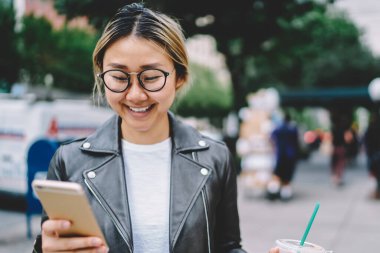 Asyalı kadın gitmek için kahve tutan şehir merkezinde dolaşmak için mobil uygulama kullanarak gülümseyen, trendy giyim oldukça Çin hippi kız iletisini alırsınız sokak zevk iş tatilinde yürürken