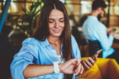 Olumlu gülümseyen hippi kız, elektronik akıllı sinyalleri takip ediyor, modern akıllı telefonu elinde tutan başarılı kadın, takılabilir kol saatine bakarken,