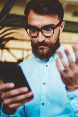 Şok olmuş sakallı hippi adam akıllı telefon cihazıyla 4G internete bağlanan bir e-posta aldı. Gözlüklü adam, modern cep telefonuyla hesap bakiyesini kontrol ediyor.